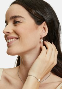 Orecchini a cerchio argentati con un design floreale che presenta tre accenti in perle, insieme a un delicato braccialetto in argento con dettagli floreali abbinati.