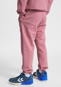 Roze katoenen trainingsbroek met elastische boorden en zijzakken, gecombineerd met blauwe en grijze sportschoenen met witte accenten.