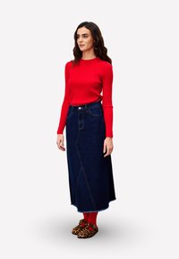 Rotes geripptes Langarmoberteil, dunkelblaue Denim-Maxikleid mit einer vorderen Naht und braunen Leopardenmuster-Schuhen. Rote Socken sichtbar.