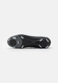 Semelle de chaussure de sport noire avec une surface texturée, comportant six crampons transparents et un accent logo circulaire près du talon.
