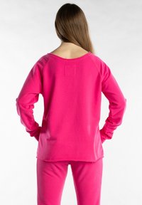 Felpa fucsia con maniche lunghe, collo ampio e vestibilità comoda. Presenta orli grezzi e una piccola toppa di tessuto sul retro.