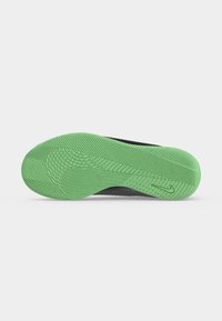 Πράσινη υφασμάτινη σόλα μαύρου παπουτσιού Nike με μικρό λογότυπο swoosh κοντά στη φτέρνα σε απλό ανοιχτογκρι φόντο.