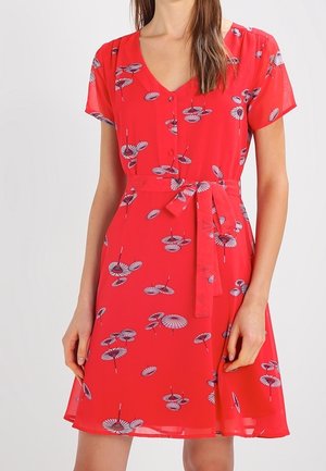 Rode jurk met korte mouwen en bloemen- en parapluprints, voorste knoopsluiting, V-hals en een ceintuur die in een strik is vastgebonden, gedragen door een staand persoon.