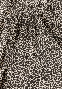 Tejido de estampado de leopardo en beige y negro, con cintura elástica fruncida, textura suave y pequeñas manchas de formas variadas por todo el diseño.