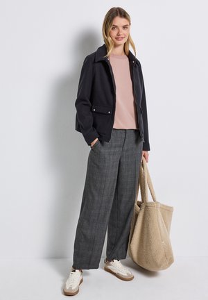 Giacca blu scuro con colletto, camicia rosa, pantaloni larghi grigi a quadri, e una borsa a tracolla beige texturizzata. Le sneakers sono color crema con dettagli marroni.