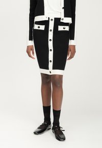 Schwarzer und weißer Strickrock mit geradem Schnitt, ausgestattet mit einer vorderen Knopfleiste und zwei vorderen Taschen mit goldenen Hardware-Details.