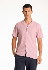 Korte mouwen button-up overhemd in lichtroze textuurstof met een camp kraag en witte knopen, gedragen met marineblauwe broek.