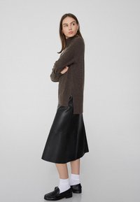 Sweater de punto marrón con cuello alto, combinado con una falda midi de cuero negra. El conjunto incluye calcetines blancos y mocasines negros.