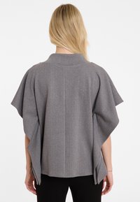 Grijze, gestructureerde cape met korte mouwen, voorzien van verticale strepen en een hoge kraag. Het ontwerp is relaxed en gestructureerd aan de achterkant.