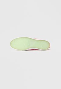 Guminės sportbačio pado dalis su permatomu žaliu dugnu, balta vidurine dalimi ir raudonu viršutiniu sluoksniu, kuriame yra keli maži oro skylutės.