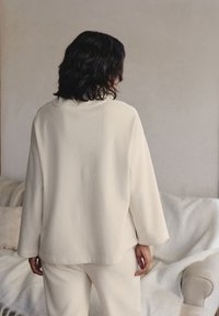 Maglione oversized di colore crema, a costine, con collo alto, maniche lunghe e vestibilità rilassata, abbinato a pantaloni coordinati.
