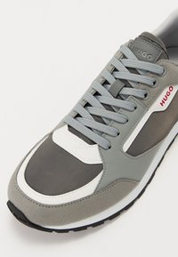 Gray athletic shoe featuring mixed materials: suede, mesh, and rubber. White accents and gray laces. Logo visible on the tongue.
