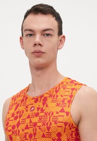 Ujj nélküli sporttop élénk narancs és piros geometrikus mintával, különböző formákkal; kerek nyakkivágás és logó részlet a mellen.