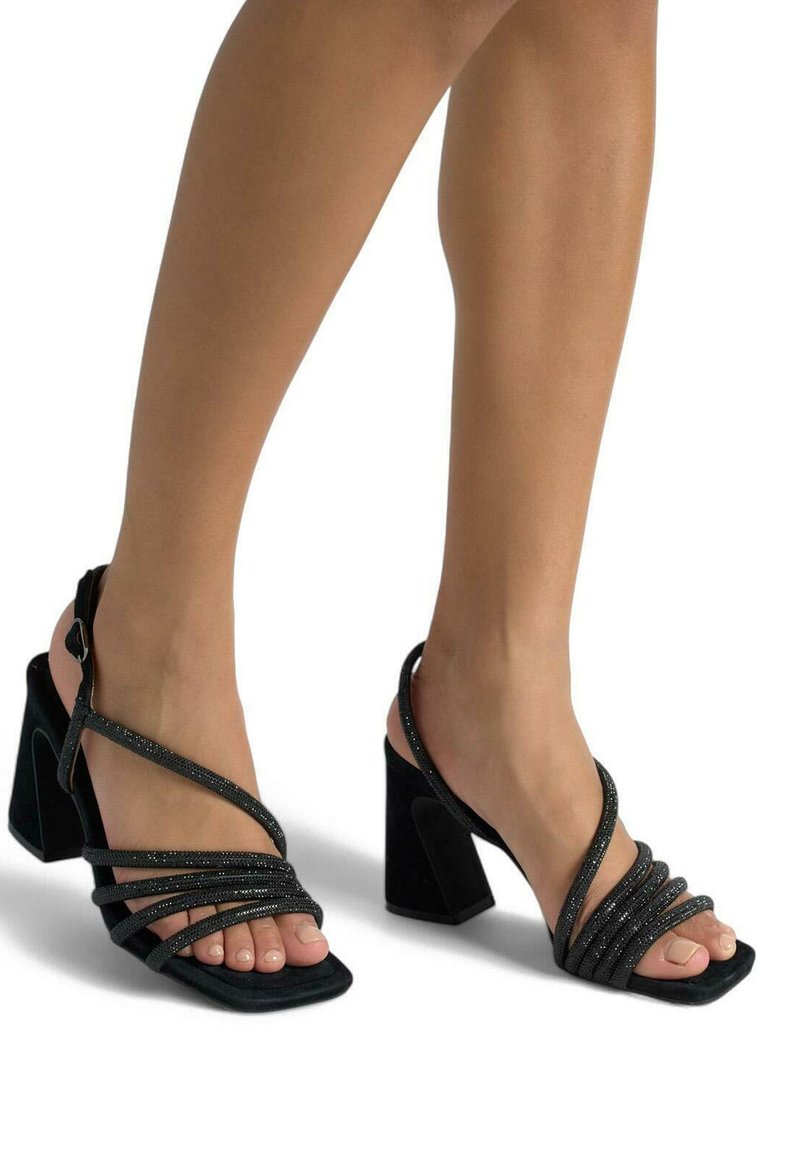 Schwarze High Heels Sandalen mit einem dicken Absatz, die über mehrere kreuzende Riemen und eine weiche Wildlederoberfläche verfügen. Offene Zehen-Design.