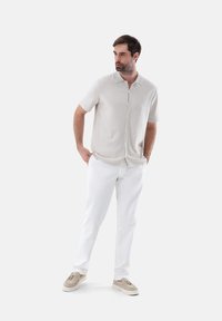 Camicia button-up a maniche corte color beige chiaro abbinata a pantaloni bianchi e scarpe slip-on beige, caratterizzata da una vestibilità comoda e una texture liscia.