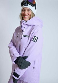 Lyslilla skijakke med justerbar hætte, sorte accenter, to frontlommer og sorte handsker. Modellen bærer en hvid hue og skibriller.