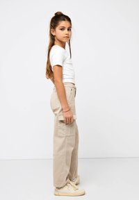 Top bianco a maniche corte abbinato a pantaloni cargo beige chiaro con tasche laterali. Le calzature sono sneakers beige, mentre i capelli sono acconciati in un semi- raccolto morbido.
