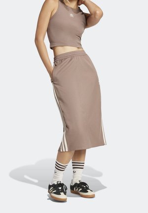 Hnědý dvoudílný outfit skládající se z upnutého crop topu a sukně po kolena s bílými bočními pruhem. Doplněný černo-bílými teniskami.