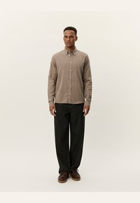 Lichtbruine knopjesoverhemd met lange mouwen, gecombineerd met donkere wijde jeans en bruine veterschoenen. Glad textuur, eenvoudig ontwerp.