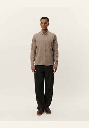Chemise boutonnée marron clair à manches longues, associée à un jean large noir et des bottes à lacets marron. Texture lisse, design simple.
