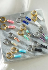 Kleurige sleutelhangers met rechthoekige pendants in roze, blauw, groen en zwart, gemonteerd op gouden en zilveren metalen ringen, tentoongesteld op een stenen oppervlak.