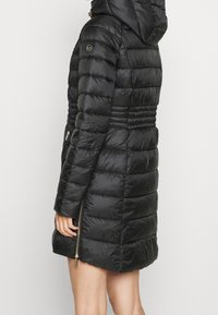 Schwarze, gesteppte Winterjacke mit Reißverschluss vorne, Kapuze und elastischer Taille. Verfügt über eine gesteppte Struktur und Seitentaschen mit goldfarbenen Beschlägen.