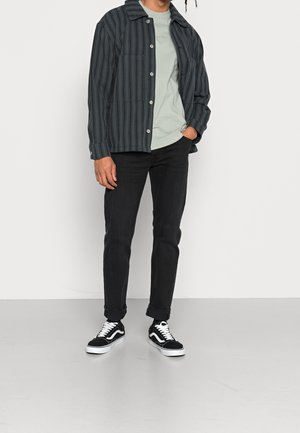 Stripet mørkeblå knap-op jakke over en mintgrøn t-shirt, kombineret med sorte jeans og sort-hvide sneakers. Casual outfit med lommer.