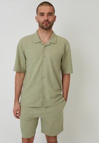 Lichtgroen polo shirt met korte mouwen en knoopsluiting, gecombineerd met bijpassende shorts. Beide kledingstukken zijn gemaakt van een textuurstof.