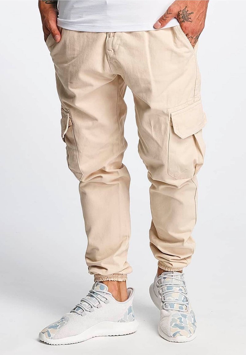Beige cargo bukser med elastiske manchetter og sidelommer; parret med lysegrå sneakers med et blåt camouflagemønster.