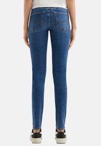 Kapeet siniset denim housut, joissa on kaksi takataskua. Kangas on sileä ja siinä on hienovarainen haalistunut pesu syvyyden saavuttamiseksi.
