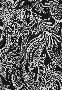 Svart tyg med intrikata vita paisley- och blommönster. Sträv yta med en mjuk finish. Inkluderar en bakfickadetalj.