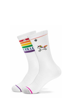 Deux chaussettes blanches montantes avec une texture côtelée ; l'une présente des rayures arc-en-ciel et un texte partiel "LOVE IS LO", l'autre une licorne aux ailes arc-en-ciel.