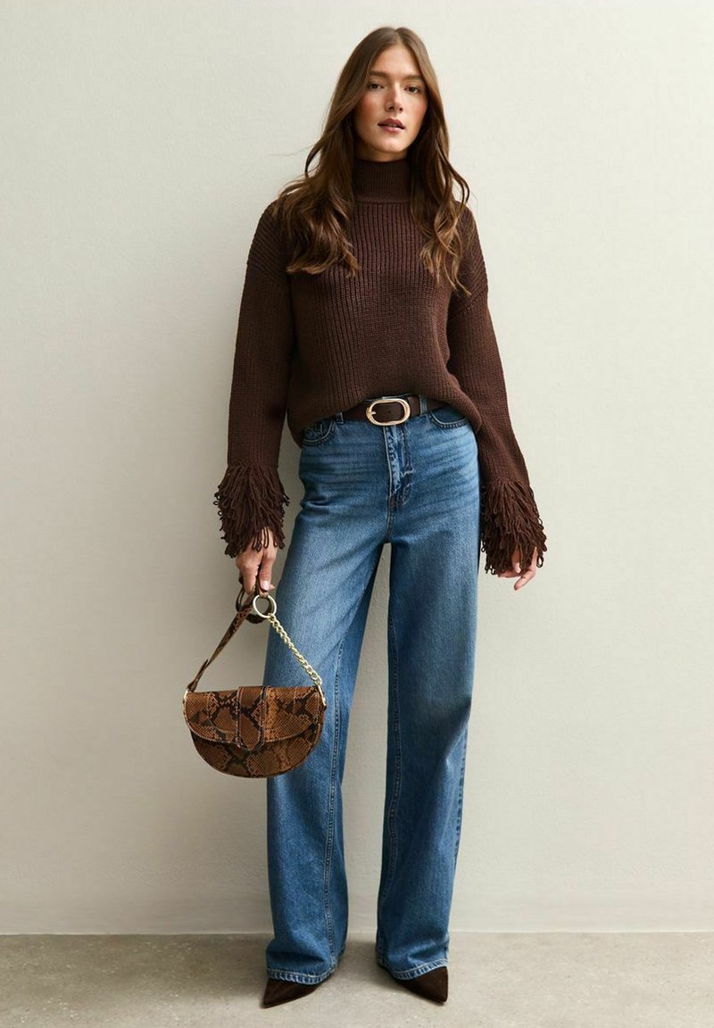 Pull en tricot marron avec des manches à franges, un jean en denim bleu taille haute et un sac à main en cuir texturé imprimé serpent marron. Talons aiguilles marron.