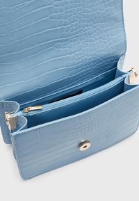 Jasnoniebieska skórzana torebka z tłoczeniem imitującym krokodyla, zamykana na magnetyczny zatrzask, z wewnętrzną kieszenią na zamek i gładką podszewką.