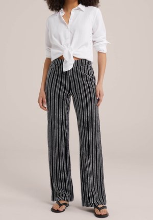 Black and white vertically striped wide-leg pants with an elastic waistband, paired with a knotted white button-up shirt. Flat sandals visible.
