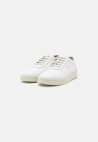 Zapatillas blancas de cuero con punta redondeada, suela de goma beige y cordones beige. Presentan un logo sutil y detalles cosidos en el lateral.