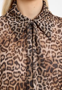 Woman wearing sheer leopard print blouse with a large pointed collar and tied neck detail, showing upper chest and neck.