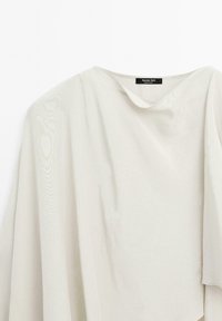 T-shirt gris clair, ample, avec un design drapé. Texture douce, décolleté en V peu profond et manches larges. Étiquette indiquant "Massimo Dutti."