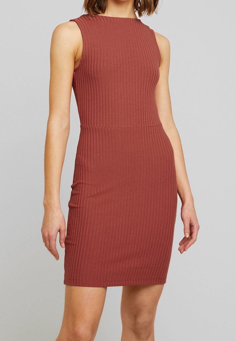 Robe sans manches moulante de couleur rouille, en tissu côtelé. Elle présente un col rond et une silhouette jusqu'aux genoux.
