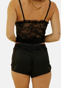 Crop top en dentelle noire avec des bords festonnés, associé à un short noir brillant avec des accents en dentelle sur les côtés.