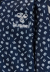 Marineblauwe stof met een herhaald patroon van lichtblauwe gestileerde letters en cijfers. Bevat een geborduurd "hummel"-logo met een bijontwerp.