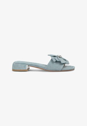 Sandalias de ante azul claro deslizantes con tacón plano, que presentan un prominente detalle de flor y un acento metálico decorativo en el lateral.