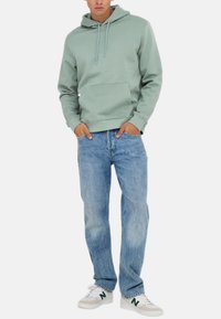 Mintgrøn bomulds-hoodie med snører, frontlomme, parret med lyseblå denimjeans og hvide sneakers med grønne detaljer.