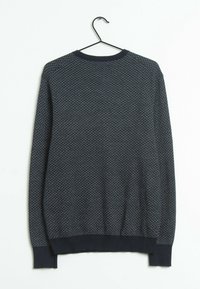 Ciemnoniebieski sweter z wzorem w jodełkę, z prążkowanymi mankietami i okrągłym dekoltem. Wisiał na czarnym wieszaku na jasnym tle.