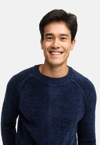 Granatowy sweter dzianinowy o teksturowanej powierzchni, z okrągłym dekoltem i rękawami raglanowymi. Tkanina jest miękka i ma regularny krój.
