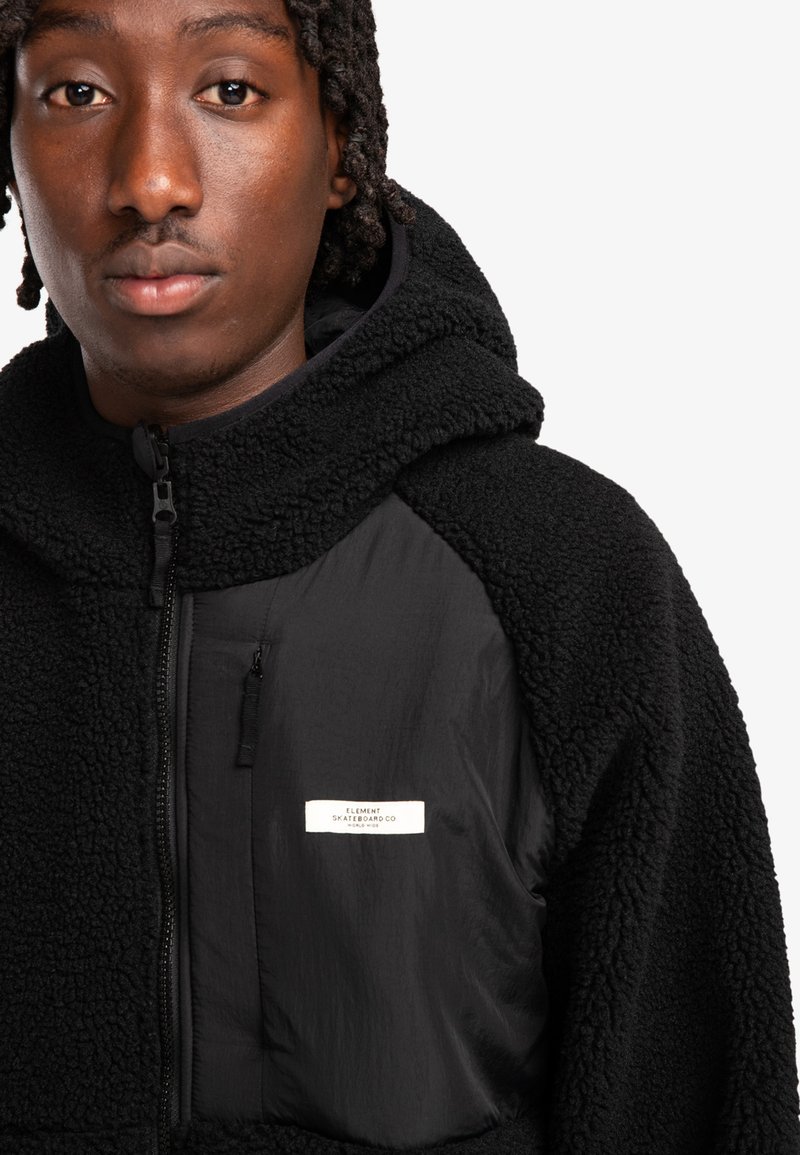 Felpa con cappuccio nera in pile, con un esterno texturizzato, dettagli in nylon lisci, tasche con cerniera e un'etichetta con la scritta "ELEMENT SKATEBOARD CO."