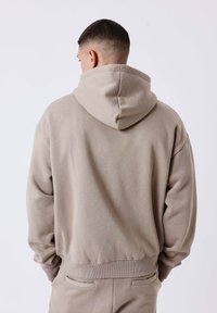 Hoodie in lichtbeige, gemaakt van zacht materiaal. Kenmerken ribgebreide manchetten en zoom, met een relaxte pasvorm en een kangoeroezak.