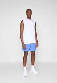 Hvid atletisk ærmeløs skjorte, blå shorts, hvide sokker og hvide sneakers, der fremviser et sporty design og en afslappet pasform.