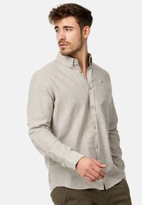 Lys beige langærmet skjorte med knapper, der har en subtil tekstur, krave og logo på brystet. Har knapmanchetter og lige kant.
