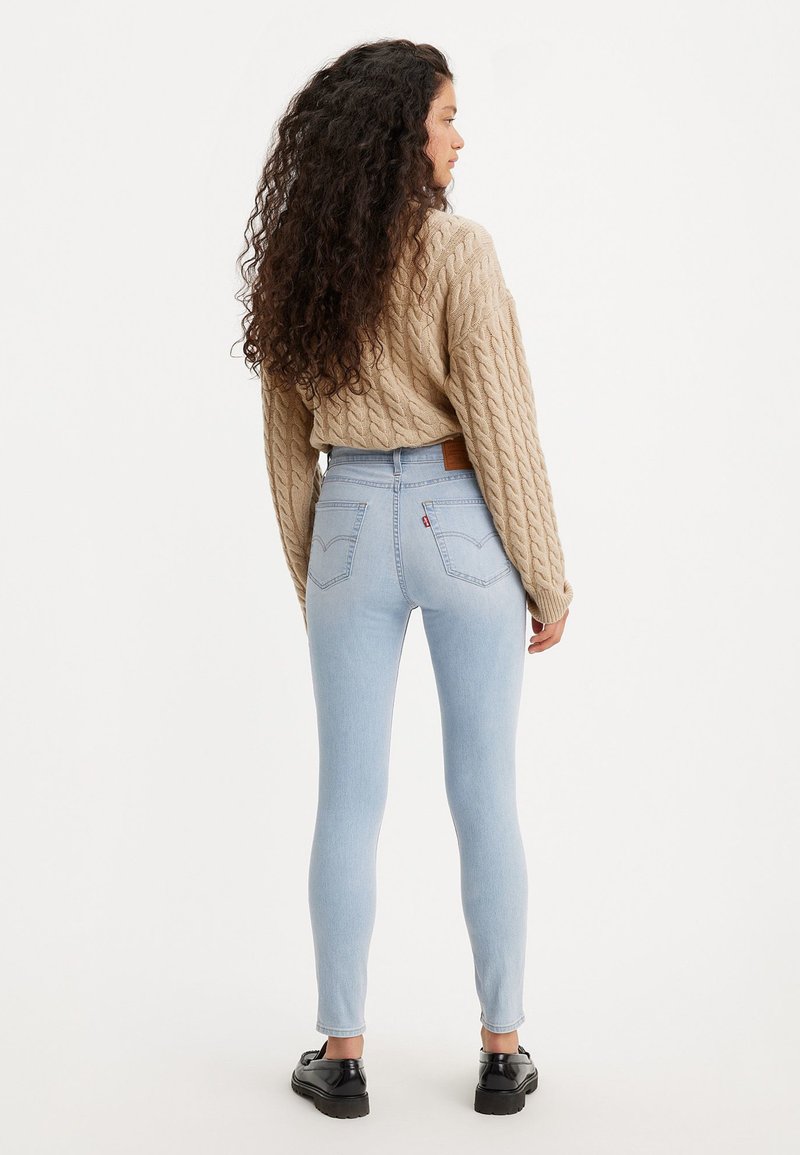 Jean skinny bleu clair à taille haute, associés à un pull beige en maille torsadée texturée et des chaussures noires. Vue de dos.